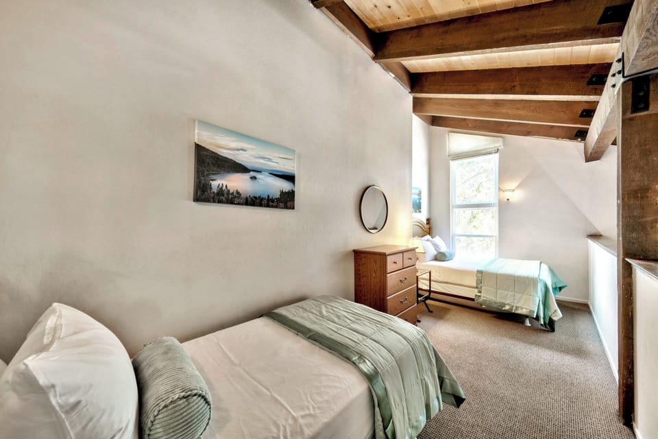 Unwind in your serene bedroom with rustic wood beams overhead and peaceful mountain artwork creating the perfect retreat.