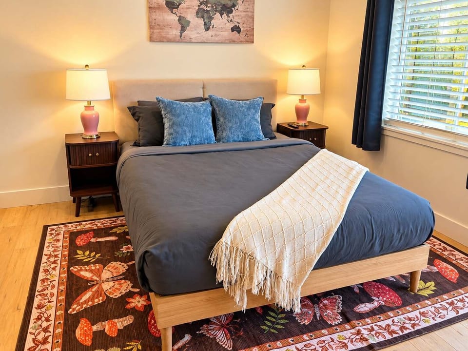 Private room with queen sized bed, nightstand charging ports, and blackout curtains.