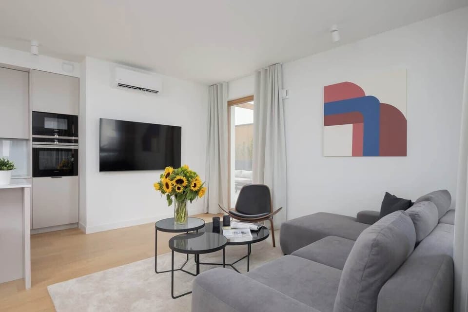 Spacious living room with grey sofa, wooden floors, TV, and open-plan layout connected to kitchen and dining space.