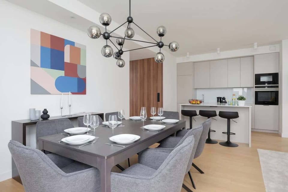 Modern living room with grey dining chairs, colorful wall art, large windows, and open layout.