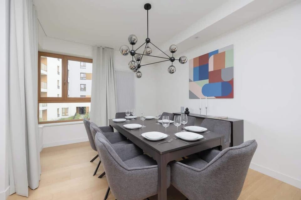 Modern living room with grey dining chairs, colorful wall art, large windows, and open layout.