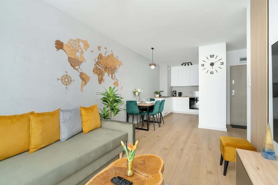 A spacious and inviting living room combining warm wood textures with a bold green sofa and floor-to-ceiling curtains, complemented by a large TV and tasteful décor.