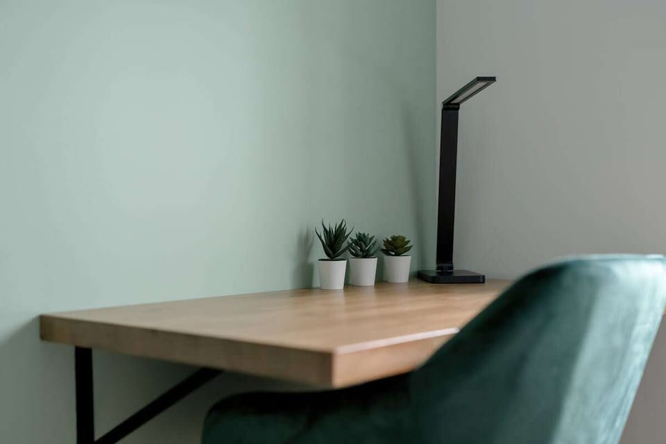 A practical home office corner with a compact wooden desk, modern green chair, and a sleek black reading lamp, perfect for focused work or study.
