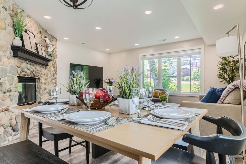 Enjoy meals in this modern dining area featuring a large wood dining table, place settings, and natural light.