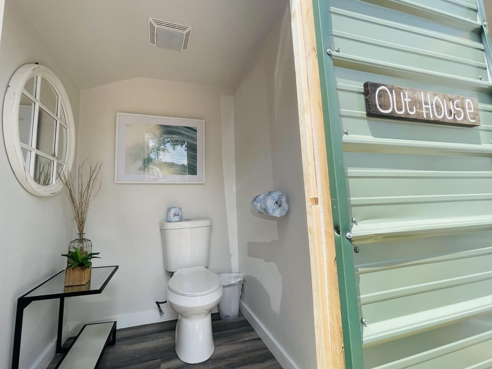Communal bathhouse features 2 separate stalls with porcelain flushing toilets &amp; hand-sanitizer. Outside is a hand-washing sink.