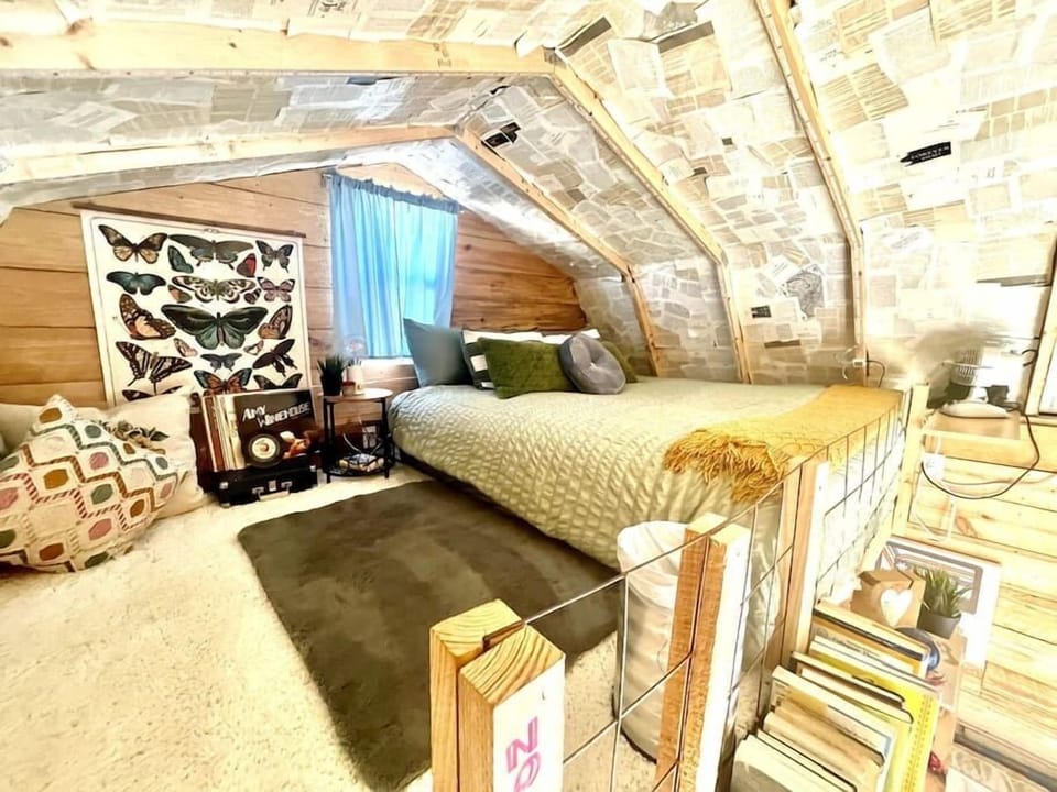 Loft bedroom under a sloped ceiling lined with vintage book pages, featuring a bed with quilted cover and butterfly wall art.