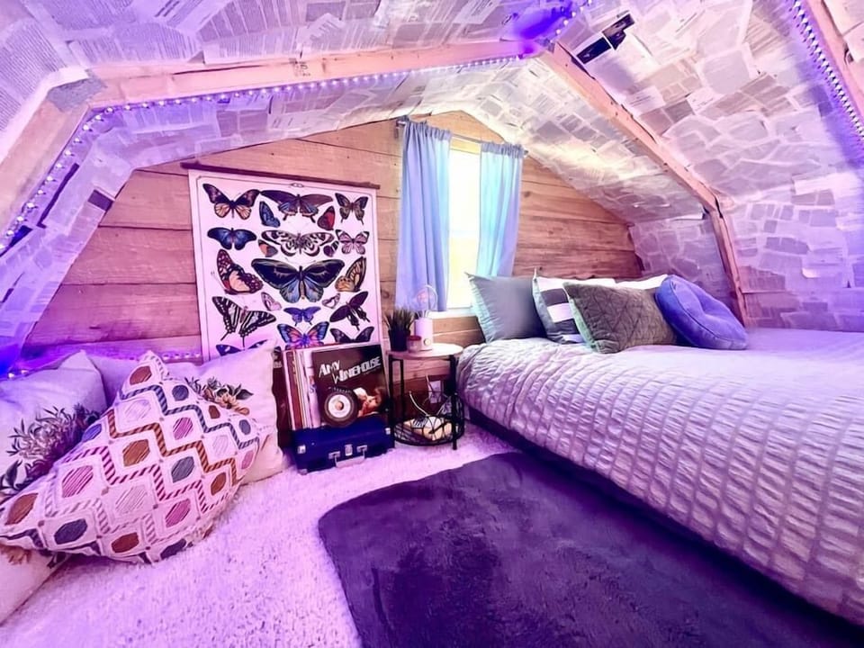 Plush rugs cover the loft floor beside a small nightstand, decorative records, patterned pillows, and butterfly wall art.