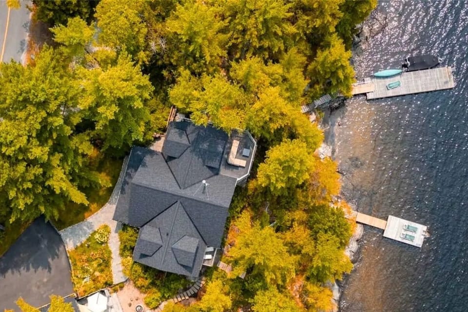 An aerial shot capturing the cottage surrounded by vibrant fall foliage, with shades of orange, red, and yellow creating a picturesque landscape.