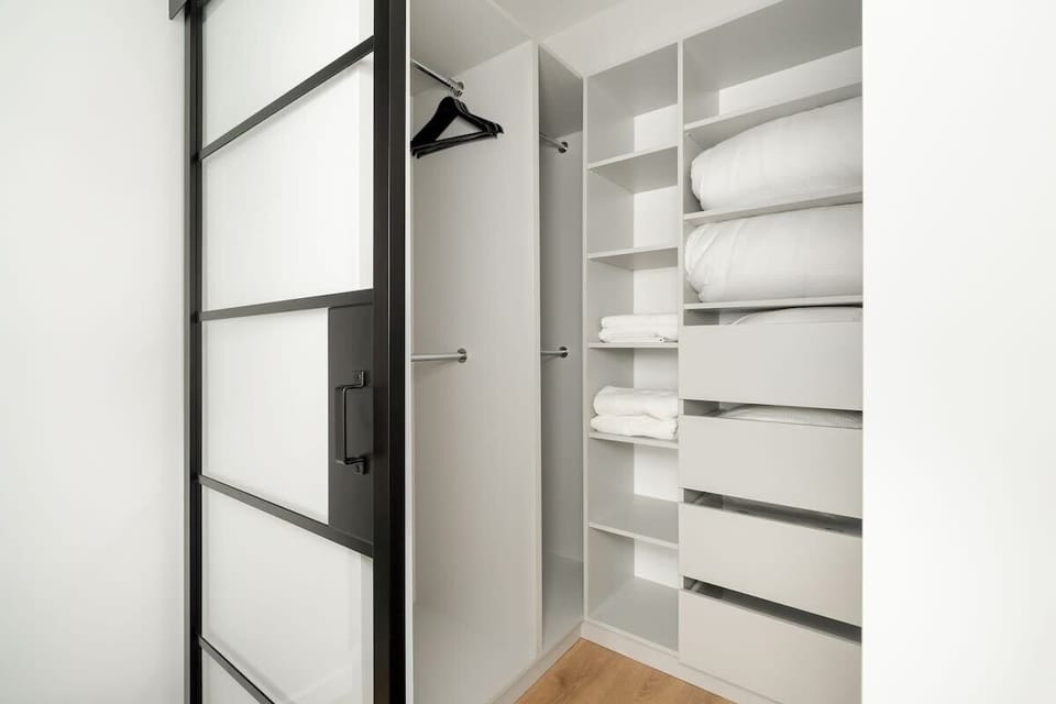 A minimalist white closet with open shelving and sliding black-framed doors. The room is clean and practical.