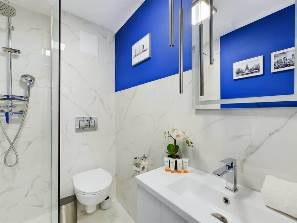 A compact bathroom with a walk-in shower, white walls, and blue cabinets. A small plant and clean finishes create a fresh atmosphere.
