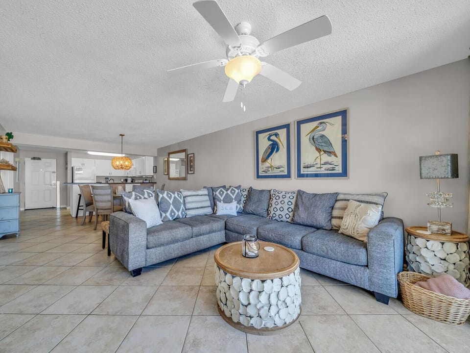 Relax on your spacious sectional sofa while the ceiling fan keeps you comfortable in this bright, coastal-themed living space.