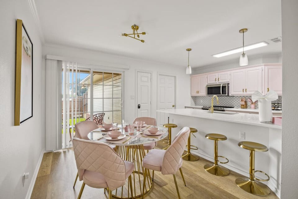 Our stylish dining area and kitchen! Enjoy meals at a chic marble table with blush pink chairs, or relax at the breakfast bar with gold stools. The bright, airy space features modern appliances and opens to a lovely outdoor area. Perfect for any stay