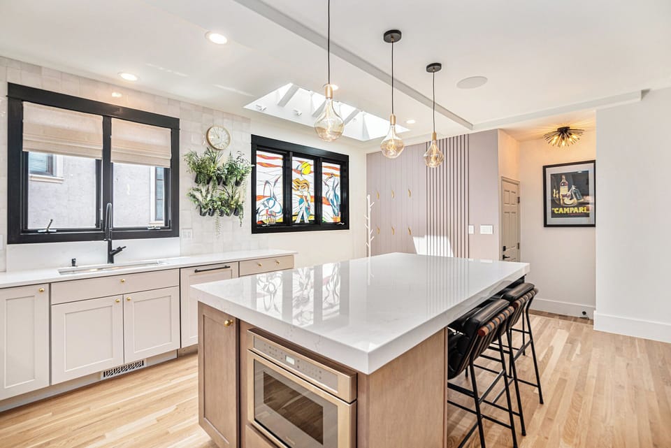 - Natural light pours in from the skylight above this spacious kitchen island
- Colorful stained glass artwork adds playful charm to the clean modern design
- Pendant lights and a built in microwave enhance functionality and flair