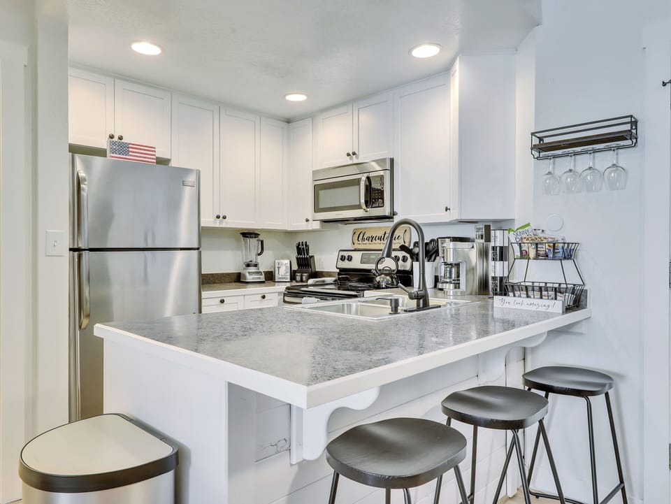 View of the Kitchen Including Microwave, Oven, Stove, Refrigerator, Stainless Steel Sink, Blender, Kettle, Crock Pot, Knife Block, Counter Seating & 3 Stools, Wine Glasses, Cooking Spices, Keurig & Drip Coffee Machine