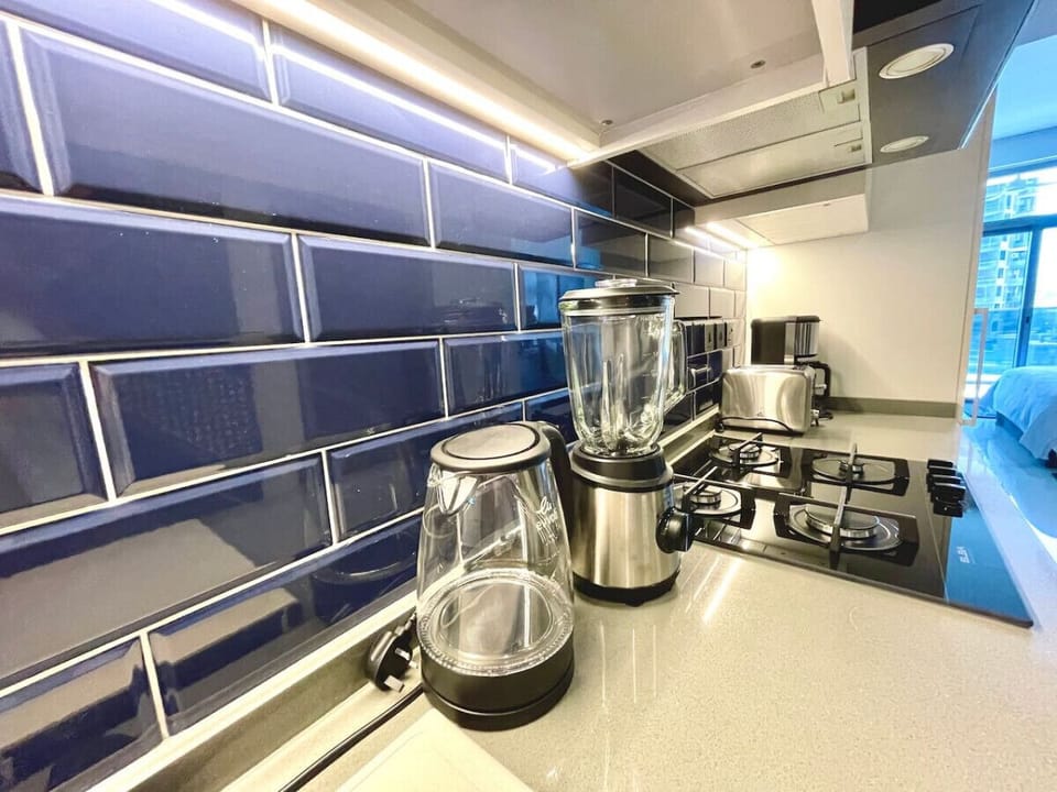 Close-up view of the stylish kitchen in a studio apartment at MAG 318, Business Bay. Showcases a luxurious blue backsplash, modern appliances including a blender, coffee maker, gas stove, and sleek counters, perfect for a vacation rental in Dubai.
