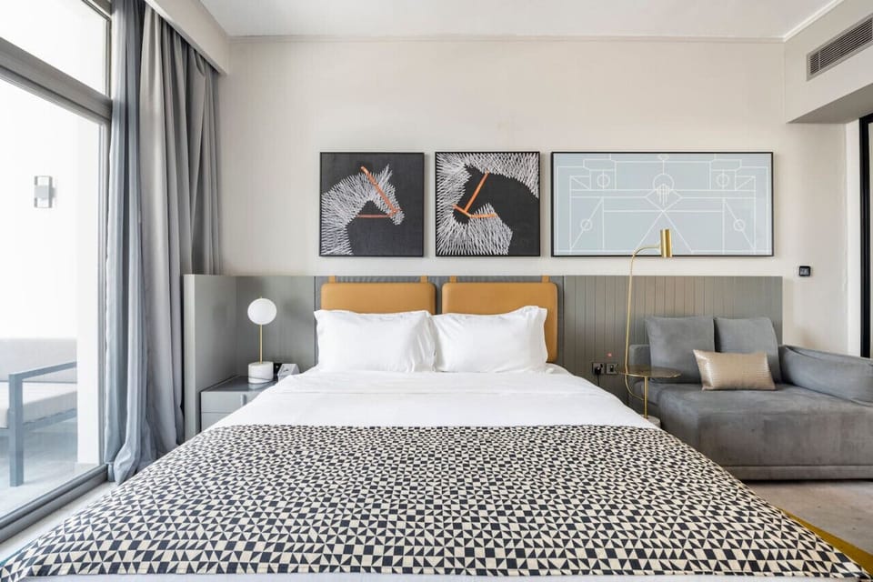 Stylish studio apartment at MAG 318, Business Bay. Features a cozy bed with chic artwork above, modern furnishings, and a balcony with views. Perfect for a vacation rental or holiday home in Dubai.