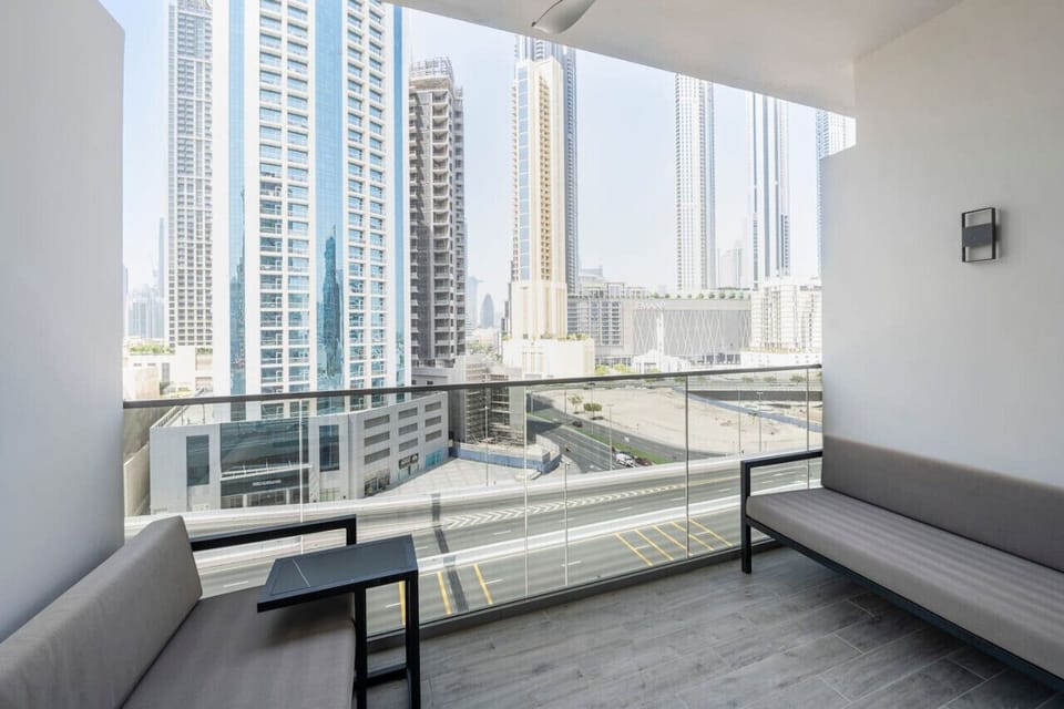 Modern balcony with seating in a studio apartment at MAG 318, Business Bay. Offers stunning city views of high-rise buildings and a bustling street below. Ideal for a short-term rental in Dubai.