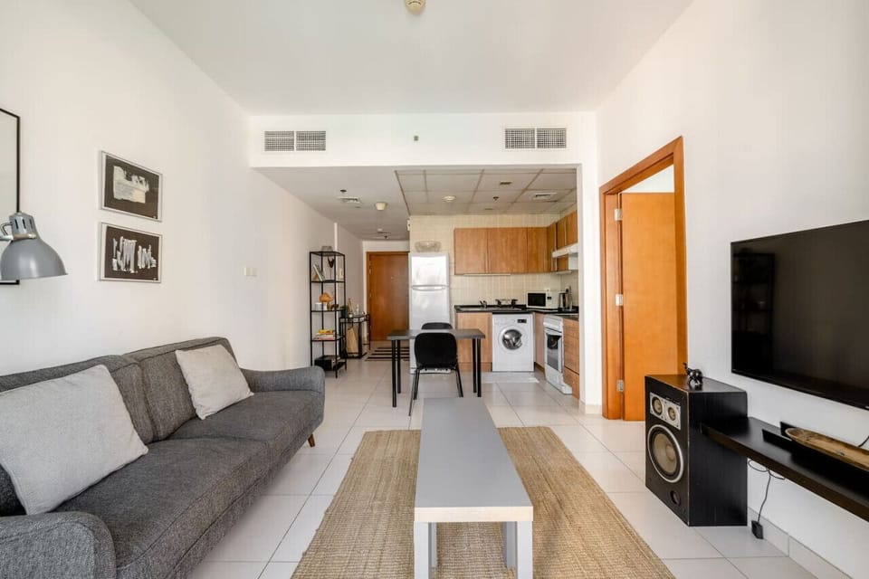 Modern 1-bedroom apartment in Marina View Tower B, featuring a stylish living space with a comfortable gray sofa, flat-screen TV, and balcony with views of Dubai Marina's skyline. Perfect for a vacation rental, short-term rental, or monthly rental in Duba