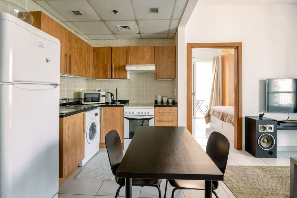 Minimalist kitchen and dining area in a 1-bedroom apartment at Marina View Tower B. Features modern appliances such as a fridge, washing machine, stove, and microwave. Ideal for holiday homes, vacation rentals, and short-term rentals in Dubai Marina.