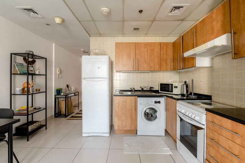 Classy kitchen view in a 1-bedroom apartment at Marina View Tower B, offering modern amenities including a fridge, washing machine, stove, and microwave. Open design for ease and comfort in a vacation rental or short-term rental in Dubai Marina. Perfect f