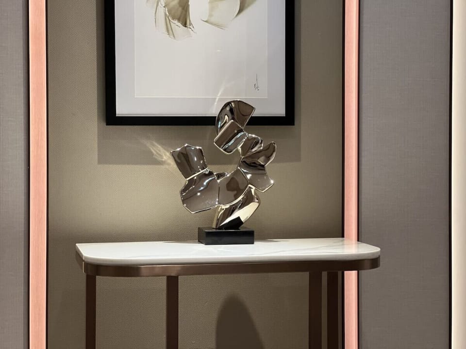 Stylish nook in Address Harbour Point Tower 1, Dubai Creek Harbour. Features a contemporary metallic sculpture on a white console table with a framed abstract artwork above. Soft, ambient wall lighting enhances the elegant decor.