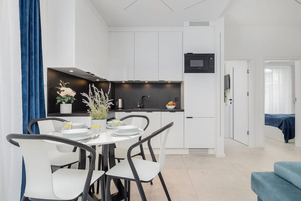 Dining Area & Kitchen – Dining area with a round table, turquoise sofa in the background, and a bright modern kitchen.

