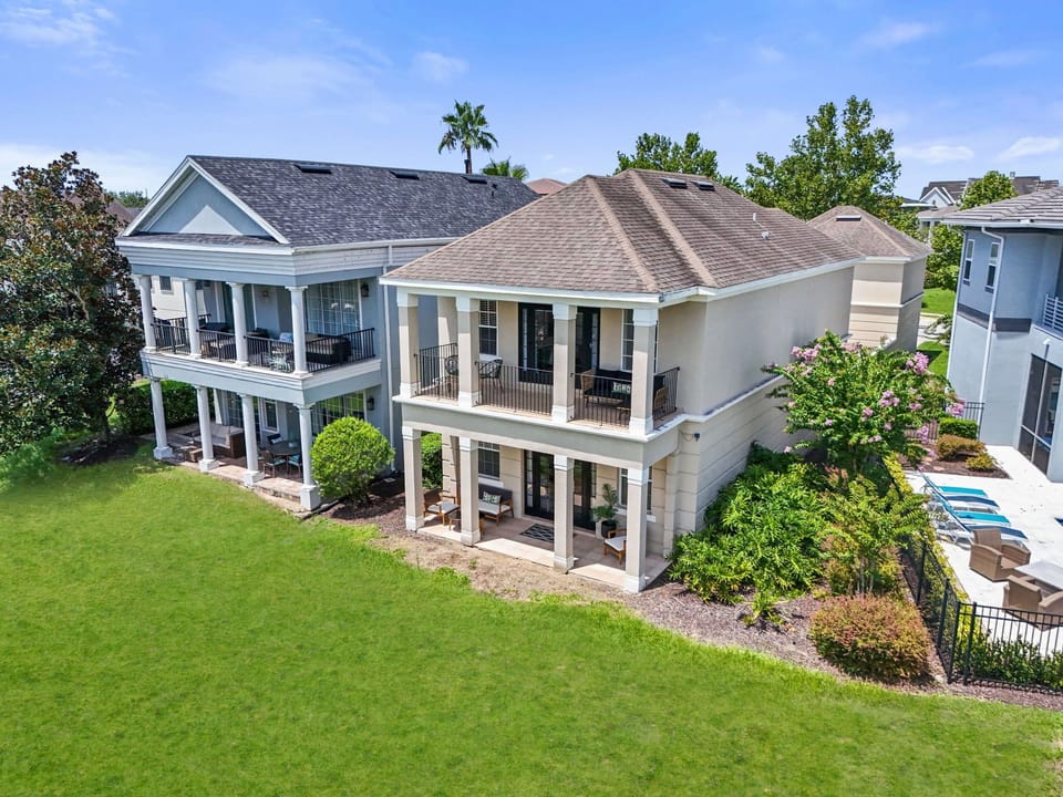 Rear exterior of the home showing expansive lawn space, balcony access, and elegant architectural details.