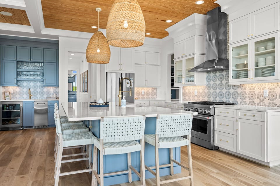 Your gourmet kitchen awaits with marble countertops, professional appliances, and coastal charm where culinary adventures unfold beneath warm woven pendant lights.