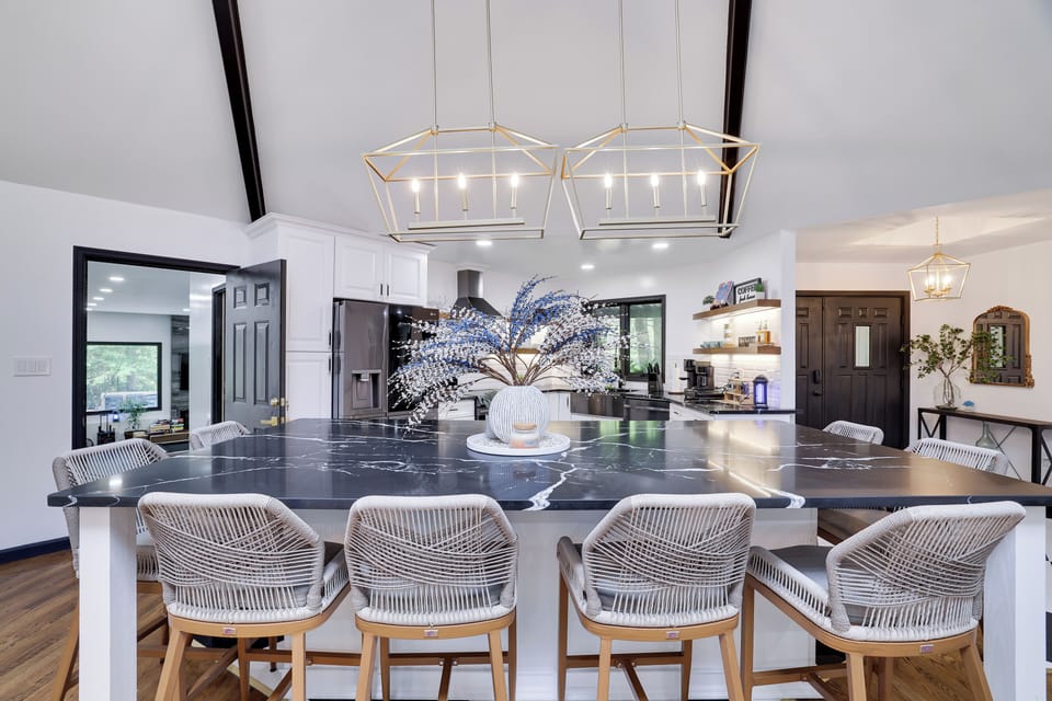 Chic kitchen with marble island, gold lights, and woven barstools.