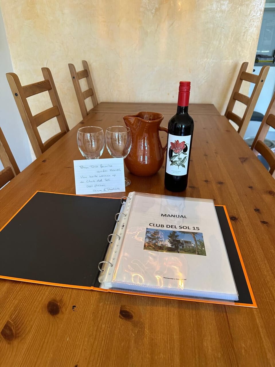 Dining table with a welcome detail: wine, glasses, a jug and the accommodation information manual.