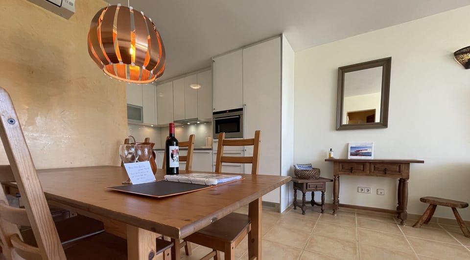 Dining area with wooden table next to the equipped kitchen, featuring a welcome detail and Mediterranean décor.