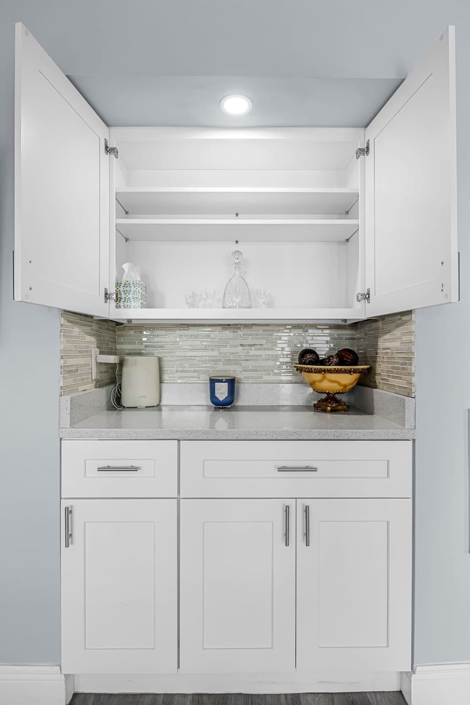 Open white kitchen cabinets with glassware and decorative items on a quartz countertop