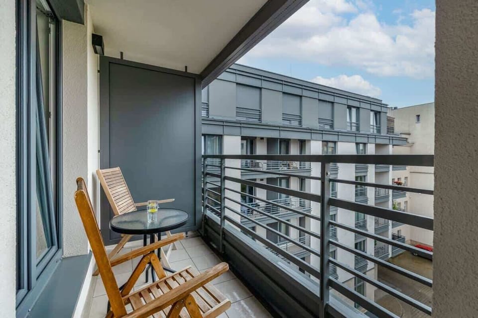 A balcony with two chairs and a small table for morning coffee. The railing overlooks nearby rooftops and trees.