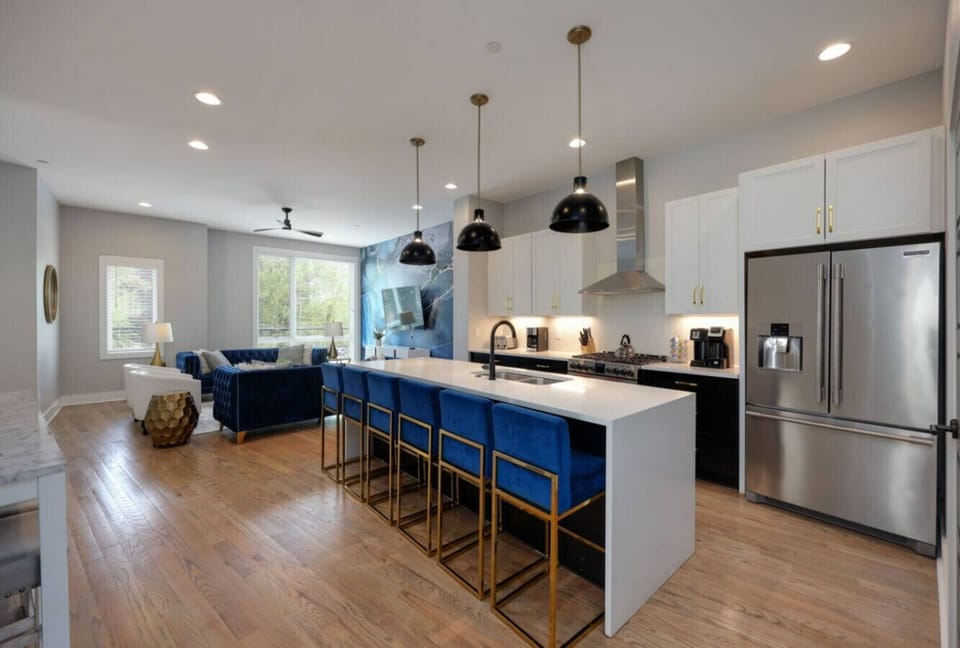 Kitchen with dark lower cabinets, white island, blue bar stools with gold legs, black industrial pendant lights