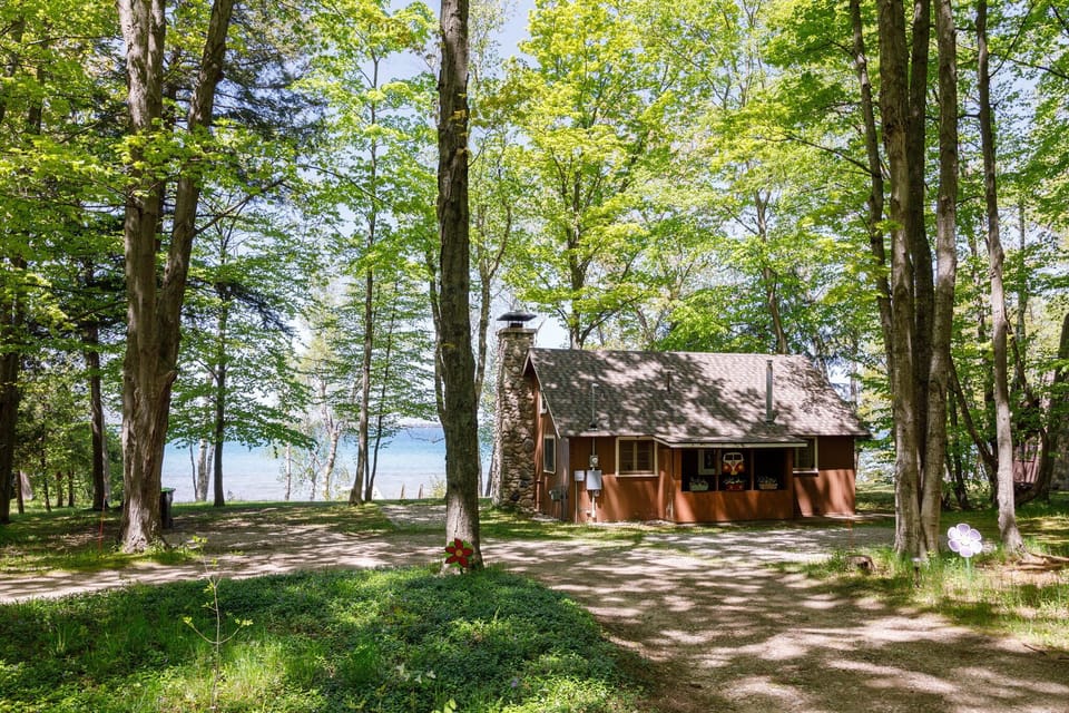 A charming cabin with a screened porch nestled among trees near a sparkling lake.