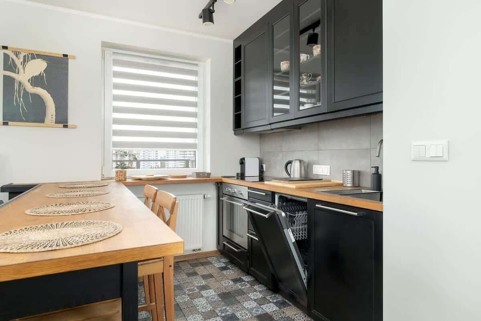 Functional kitchenette with stylish black furniture and wooden table with chairs. 