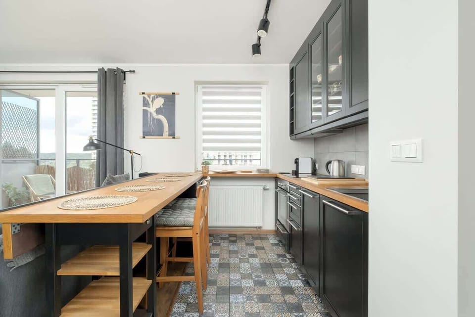 Functional kitchenette with stylish black furniture and wooden table with chairs. 