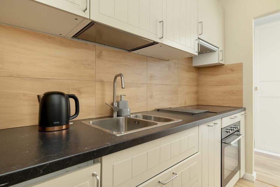 Kitchenette with light-coloured furniture and dark marble worktop. The kitchen is equipped with appliances that ensure the preparation of home-cooked meals. 