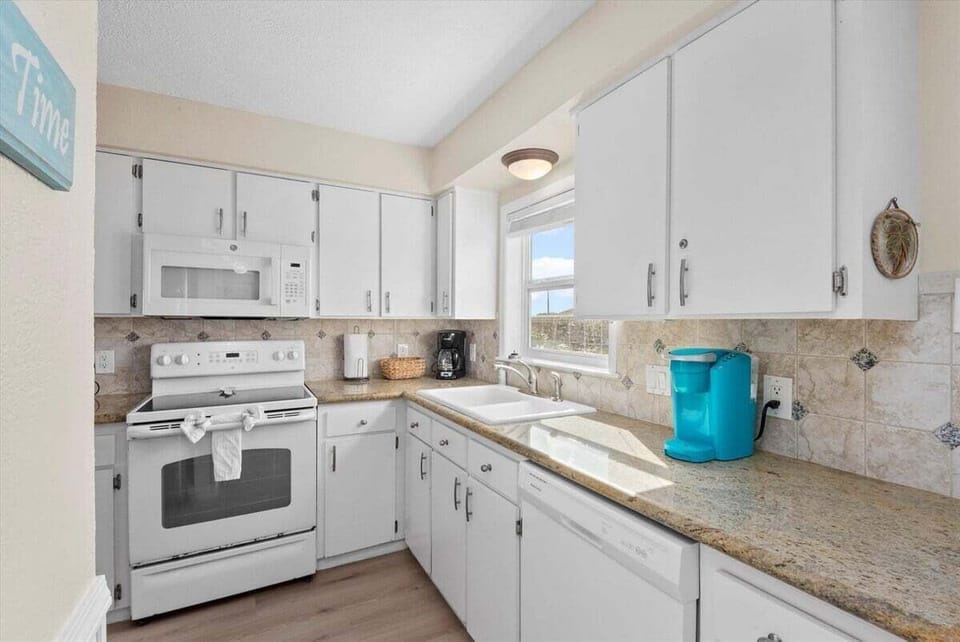 Fully equipped kitchen with white cabinetry, granite countertops, stove, and coastal design perfect for extended Galveston stays.