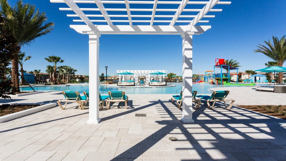 Beautiful pool area with shaded pergola, sun loungers, splash zone, and relaxing cabanas.