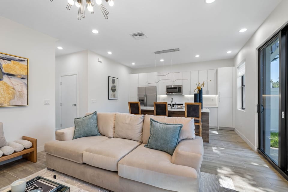 Where the neutral tones, plush furniture, and striking abstract art are beautifully complemented by statement lighting and the warmth of natural light through expansive door and windows!
