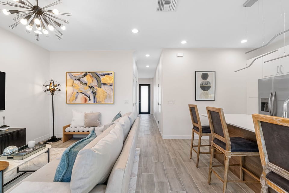 With an open-plan living space, showcasing a sleek kitchen with white cabinetry and enhanced by natural light streaming through expansive windows and glass doors leading to the backyard