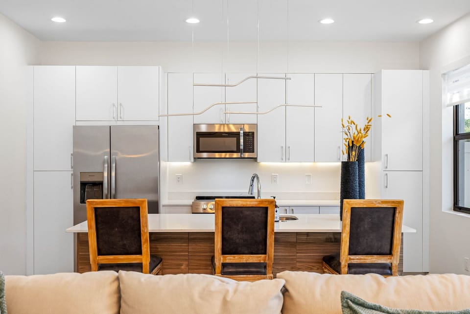 Featuring abundant white cabinetry, a central countertop with a built-in sink, and high seating for a touch of modern convenience