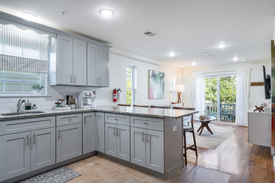 Bright and airy kitchen with natural light from a large window, well-stocked with glassware, mugs, bowls, and essentials. Includes a coffee maker, toaster, blender, and other small appliances for all your cooking needs.