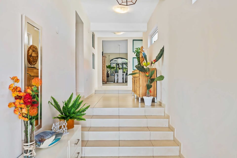 A bright hallway leads to the bedrooms, adorned with vibrant plants and decor - Steps add depth to the hallway, which features a blend of modern and rustic furnishings - Large windows and strategic lighting keep the space airy and inviting