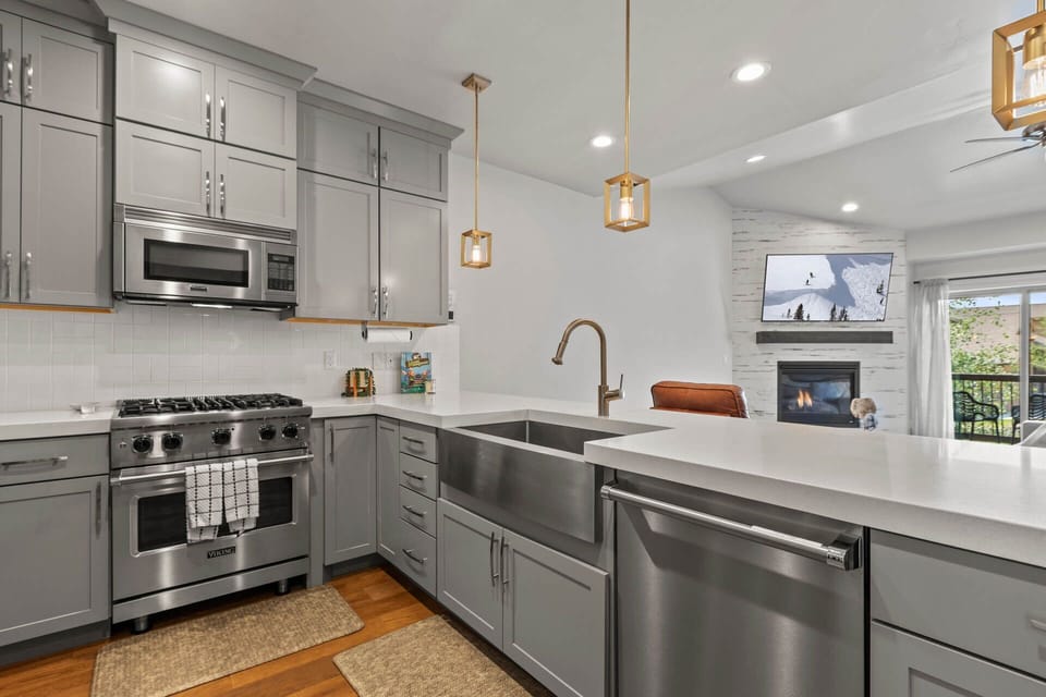 Your gourmet kitchen awaits with sleek stainless appliances, elegant quartz countertops, and a cozy fireplace visible from the chef's island—perfect for crafting meals while staying connected to your group.