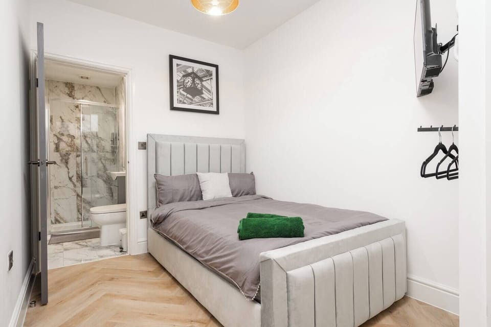 A comfortable double bedroom with a wall-mounted Smart TV, clothes hanger, and private ensuite. Fresh towels and bedding are provided for all guests, offering a clean and convenient space to relax after a day exploring Liverpool or working nearby.