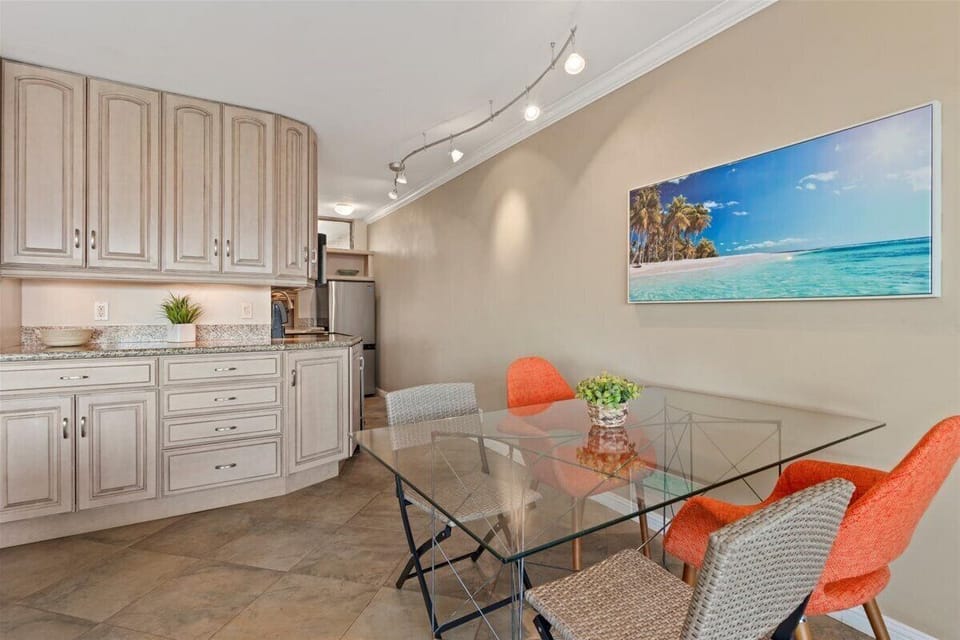 Gather around this bright dining nook where coral-hued chairs and a glass-top table invite leisurely meals and morning coffee, all brightened by coastal artwork overhead.