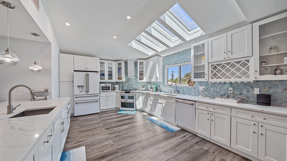 The spacious gourmet kitchen is a chef’s delight, featuring sleek white cabinetry, a striking blue coastal-themed backsplash, and an abundance of natural light for preparing delicious meals during your Sarasota stay.