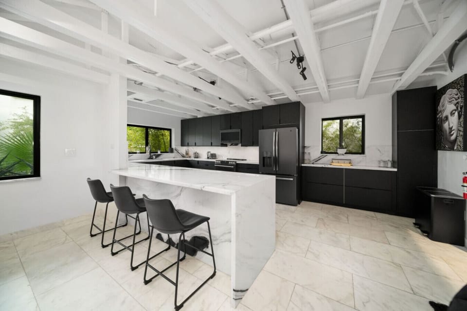 Modern kitchen with black cabinets, marble countertops, & a breakfast bar.